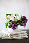Posy of lilac in white vase on folded laundry