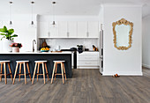 Bar stools at black island counter in white open-plan kitchen