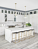 White kitchen with island counter, bar stools and glass and brass pendant lamps