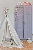 Play wigwam with sheepskin rug in front of lilac wardrobe