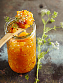 Apricot chutney in a mason jar with red peppercorns and chervil