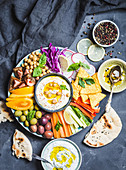 Meze-Platte mit Hummus, Joghurt-Dip, Gemüsesticks, Kichererbsen, Oliven und Pitabrot