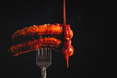 Ketchup falling on delicious grilled sausages pricked in fork