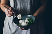 Woman with spoon in hand and holding bowl with stracciatella ice cream balls decorated with mint leaves