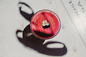 From above bubble frothy tasty fragrant pink smoothie with flowers in glass on wooden table