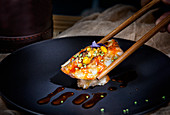 Appetizing delicious colorful sushi with red sauce and green seeds sushi with chopsticks at served table in restaurant
