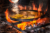Zubereitung von Paella in großer Paellapfanne über offener Feuerstelle