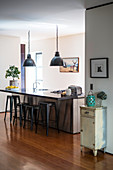 Island counter with bar stools below industrial lamps in open-plan kitchen