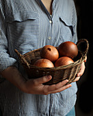 Shiny appetizing onion in peel in brown straw-plaited basket in hands