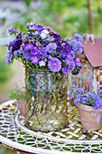 Bouquet of asters, floss flowers and verbena in glass vase on garden table