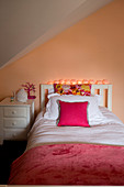 White bed and bedside cabinet in attic room with apricot wall