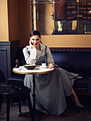 Dunkelhaarige Frau in gestreifter Hemdbluse mit kariertem Trägerkleid im Restaurant