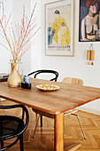 Simple wooden table and various chairs in front of art posters