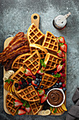 Big breakfast waffle bar served on a wooden board with berries, bacon and chocolate sauce