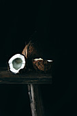 Geöffnete und und ganze Kokosnuss auf rustikalem Holzschemel