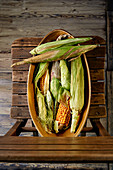 Freshly harvested corn with husks on a wooden chair