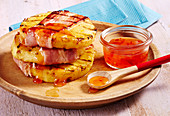 Grilled bacon and pineapple slices with a sweet and spicy chilli sauce on a wooden plate