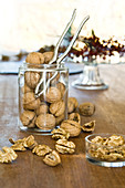 Organic walnuts, whole and cracked, in a jar with a nut cracker on a wooden table
