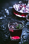Carafe and crystal glasses with ice filled with red wine on black table