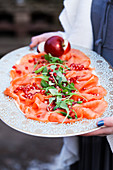 A woman holding a plate with smoked salmon and pomegranate seeds
