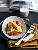 Baby banana stuffed crepes in caramel sauce with raspberries