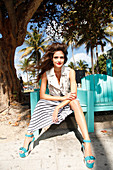 A young woman sitting on a beach chair wearing a leather gilet and a wrap-around skirt