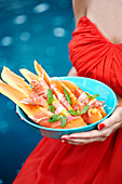 A woman holding a bowl of melon with ham