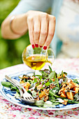Womans hand adding oil into salad