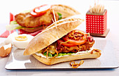A schnitzel sandwich with tartare sauce, tomato and fried onions