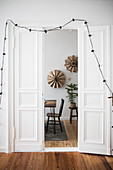 Fairy lights draped around open panelled doors in period apartment with view into festively decorated dining room