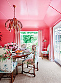 Dining room with pink wall and ceiling, round dining table and upholstered chairs with floral motifs