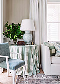 Round side table with checkered tablecloth between antique upholstered chair and sofa