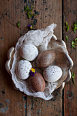 Gesprenkelte Eier auf einem Stück Mull in einer rustikalen Schale