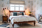 Antique wooden bed in bedroom with romantic, pale-blue floral wallpaper