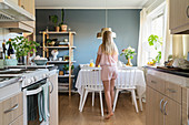 Mädchen im Pyjama deckt den Frühstückstisch vor offener Küche