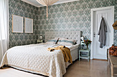 Double bed with beige bedspread and wallpaper in shades of grey in bedroom