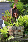 Pflanzkübel mit Farn am Wasserspeier und Dekofiguren im Garten