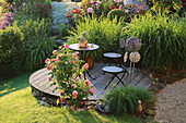 Tisch und Stühle auf Holzdeck, umgeben von Rosen und Chinaschilf im Garten