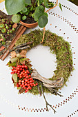 Moss wreath with viburnum berries and twigs on white metal table