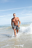 A grey-haired man with a large tattoo in the sea wearing grey swim shorts
