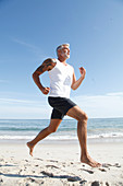 A grey-haired man with a large tattoo jogging on a beach