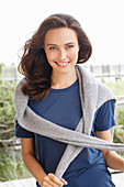 A young brunette woman wearing a short-sleeved blue t-shirt with a grey jumper around her shoulders