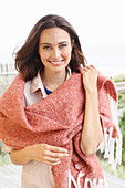 A young brunette woman wearing a light shirt blouse with a salmon pink woollen shawl