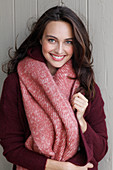 A young brunette woman wearing a wine-red cardigan with a salmon pink woollen shawl