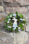 Easter wreath wrapped from moss, hay, and ivy, decorated with quail eggs, chicken feathers, and a wooden bunny figure