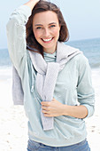 A young brunette woman wearing a light grey hooded top with a jumper around her shoulders