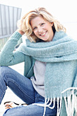 A blonde woman wearing a light knitted jumper, a woollen shawl and jeans