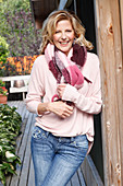 A blonde woman wearing a pink blouse, a thick scarf and jeans