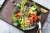 Healthy salad bowl with bean sprouts, beef, cucumber, herbs, lime, roasted peppers and tomatoes