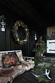 Fur blankets on garden bench and large wreath outside black wooden house